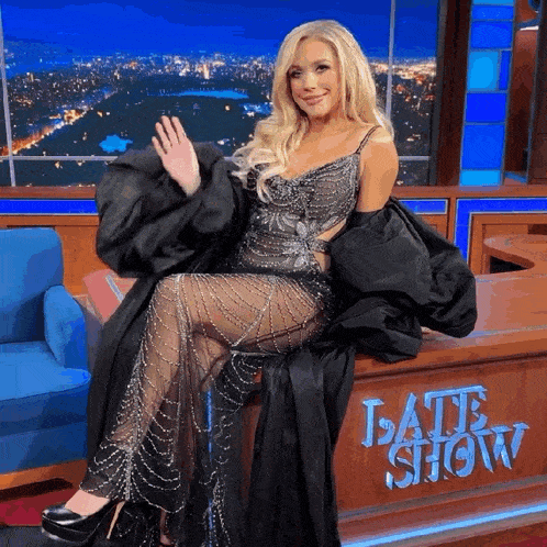 a woman in a black dress is sitting in front of the late show
