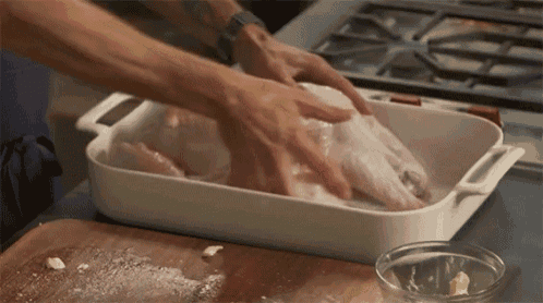 a person is putting a turkey in a white casserole dish .