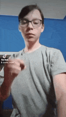 a boy wearing glasses and a grey shirt is making a tik tok video .