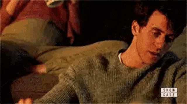 a man in a sweater is laying on a couch with a cup of coffee .