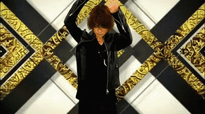 a man in a black leather jacket is dancing in front of a gold and black patterned background