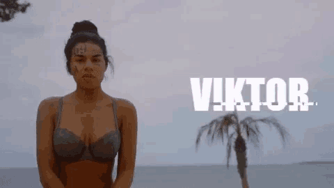 a woman in a bikini with a tattoo on her face is standing in front of a palm tree on a beach .