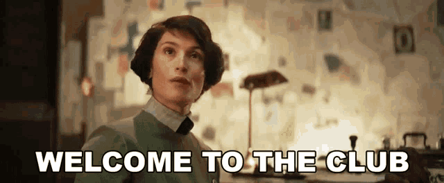 a woman says welcome to the club in front of a bulletin board