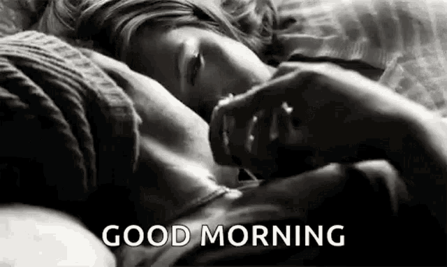 a black and white photo of a woman laying in bed with the words `` good morning '' written on the bottom .