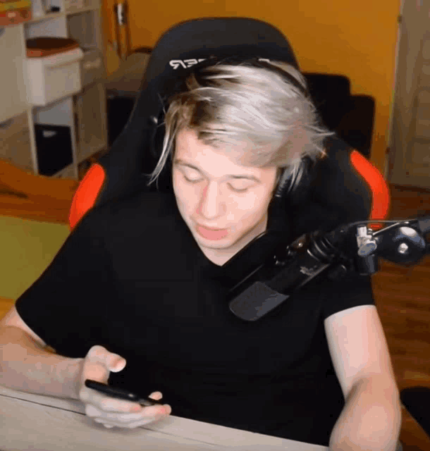 a man wearing headphones and a black shirt is looking at a phone