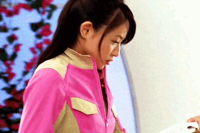 a woman in a pink jacket is standing in front of a window
