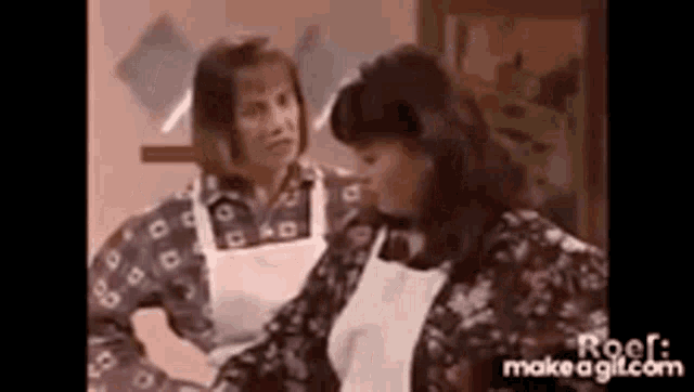 two women in aprons are standing next to each other in a room .