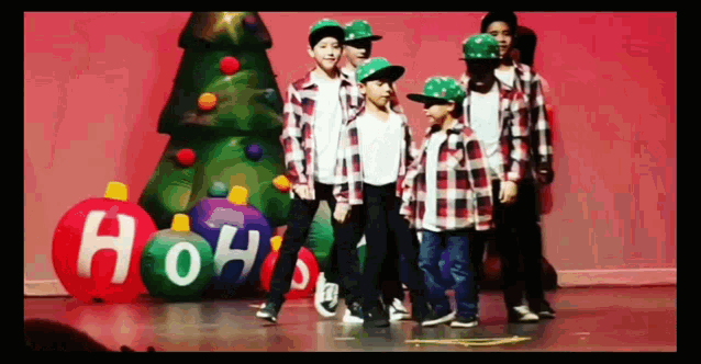 a group of young boys are dancing on a stage in front of a christmas tree