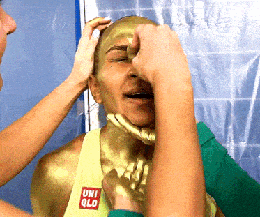 a woman with gold paint on her face is wearing a yellow tank top with the word uniqlo on it