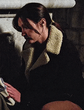 a woman in a black coat with a sherpa collar is sitting next to a man in a chair .