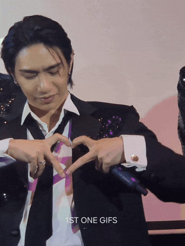 a man in a suit making a heart shape with his hands
