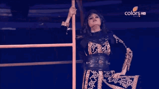 a woman in a black and gold dress is standing on a ladder with the words colors hd behind her