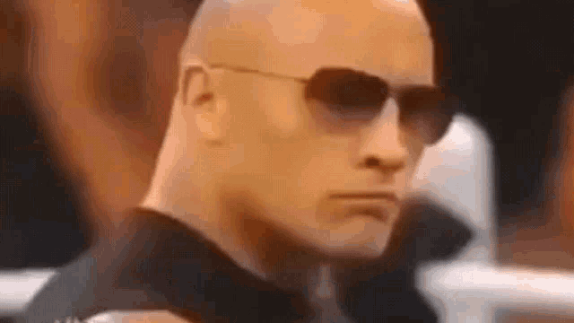 a bald man wearing sunglasses and a black shirt .