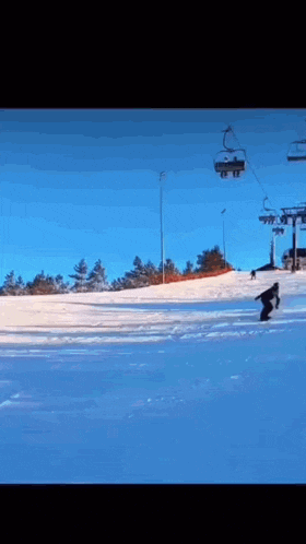 a person riding a snowboard down a snow covered slope with a ski lift in the background