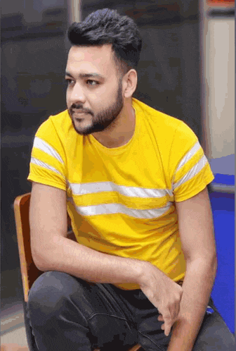 a man with a beard wearing a yellow shirt is sitting on a chair