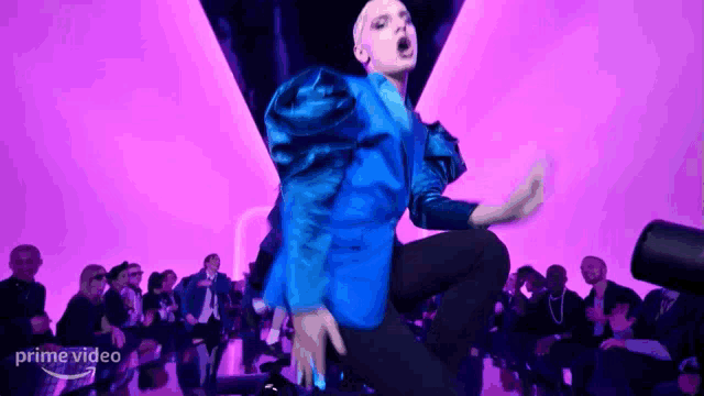 a man in a blue jacket is dancing on a stage in front of a crowd .