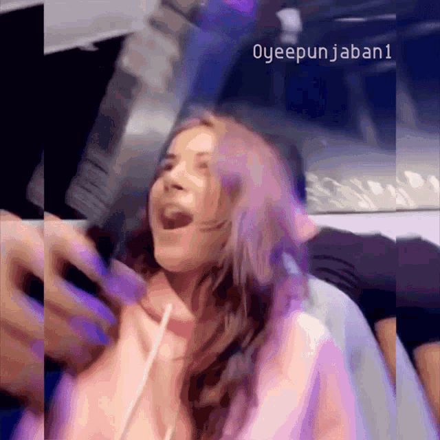 a woman in a pink hoodie is laughing with her mouth open in a video taken by oyeepunjaban1
