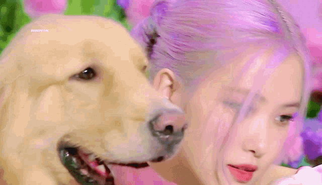 a woman with purple hair is holding a dog in front of flowers .