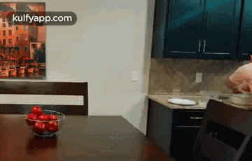 a bowl of tomatoes sits on a table in a kitchen .