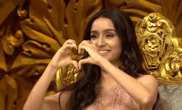 a woman in a pink dress is making a heart with her hands