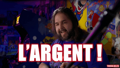 a man with long hair and a beard is playing a video game and says " l' argent "