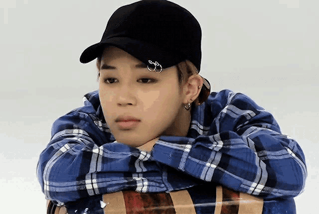 a young man wearing a blue plaid shirt and a black baseball cap