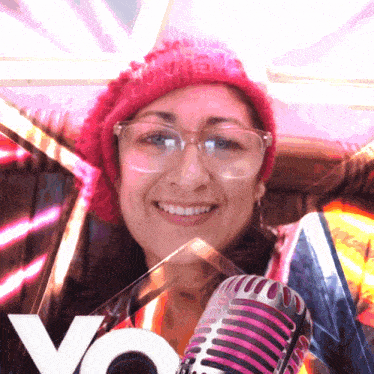 a woman wearing glasses and a red hat holds a microphone