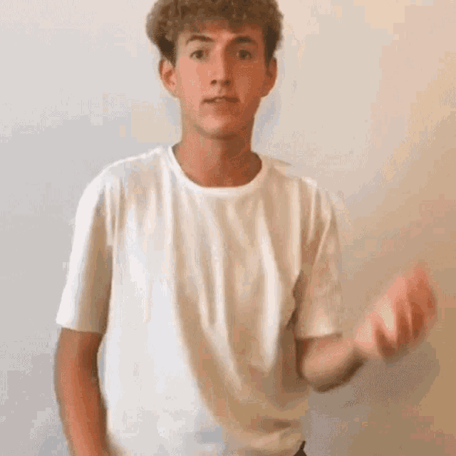 a young man wearing a white t-shirt is holding a piece of paper in his hand .