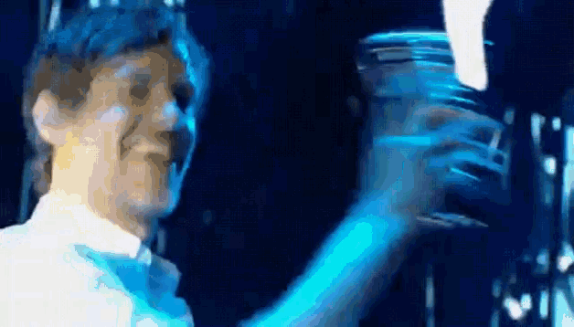 a man in a white shirt and bow tie is holding a glass of water in his hand .