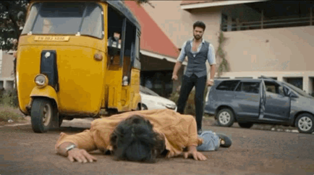 a man is laying on the ground in front of a yellow rickshaw with a license plate that says ' a '