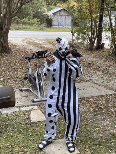 a clown in a black and white striped outfit is standing in front of an exercise bike
