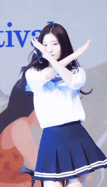 a girl in a white shirt and blue skirt stands in front of a microphone with the word live in the background