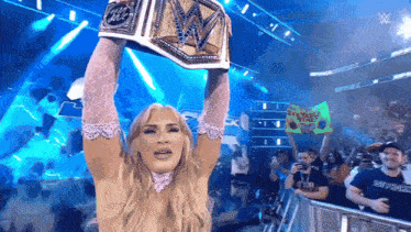 a woman is holding up a wrestling championship belt in front of a crowd