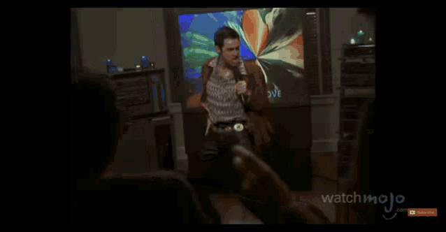 a man singing in front of a television with the words love on it