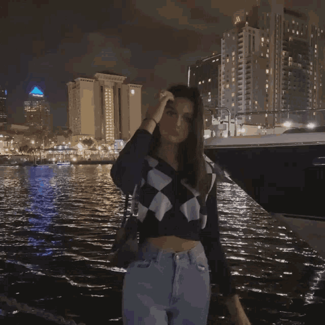 a woman in a black and white checkered sweater is standing in front of a body of water