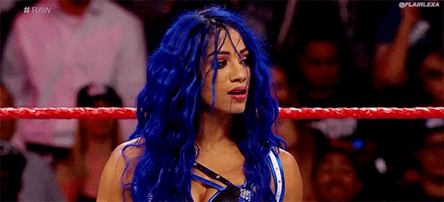 a woman with long blue hair is standing in a wrestling ring .