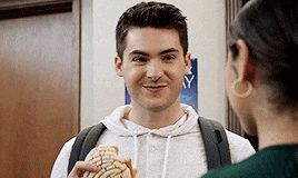 a young man is holding a concha and smiling at a woman .