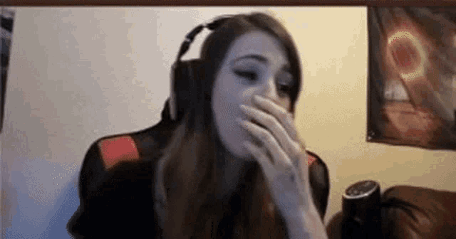 a woman wearing headphones is covering her mouth while sitting in front of a computer screen .