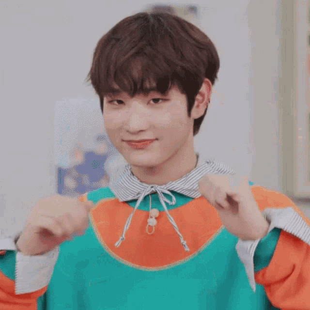 a young man is making a heart shape with his hands while wearing a colorful sweatshirt .