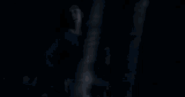 a woman in a blue shirt is standing in the dark holding a sword .