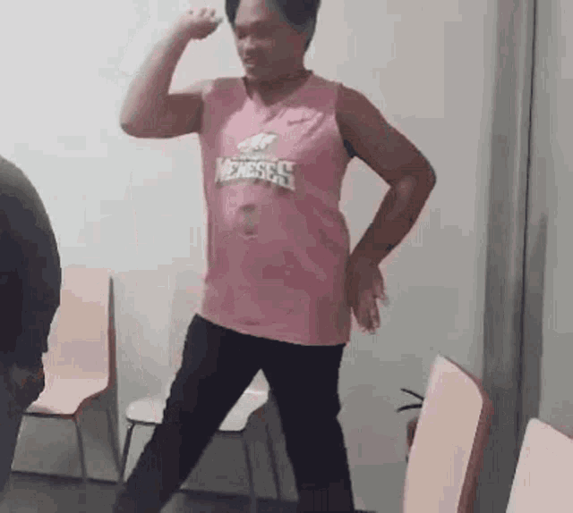 a man in a pink shirt is flexing his muscles in a room .