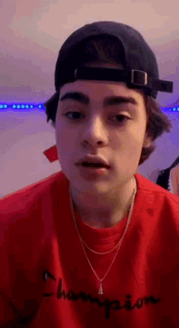 a young man wearing a hat and a red shirt is making a face .