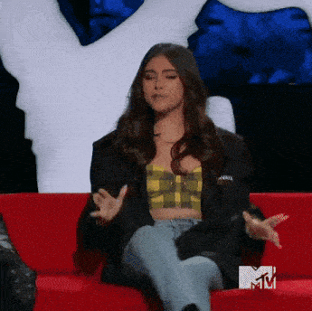 a woman is sitting on a red couch wearing a plaid top and a jacket .