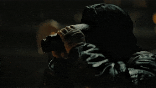 a man wearing a hat and gloves looks through binoculars in the dark