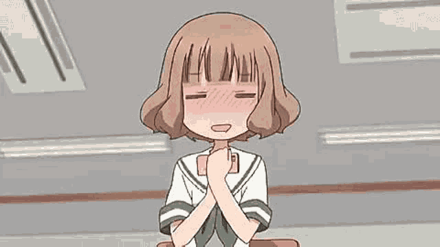a girl in a school uniform is sitting at a desk with her hands folded in front of her chest .