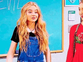 a girl in overalls stands in front of a blue board with the word evil written on it