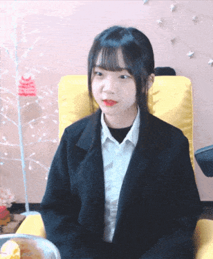 a girl in a suit sits in a chair with a christmas tree in the background