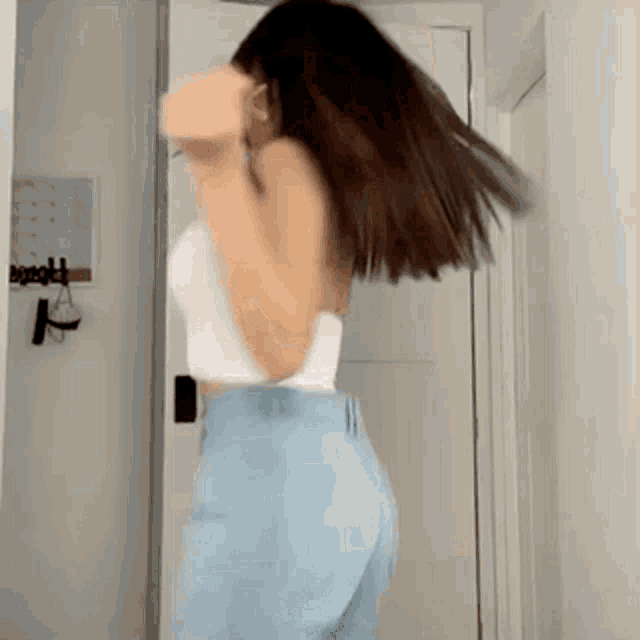 a woman in a white top and light blue jeans is dancing in a room .