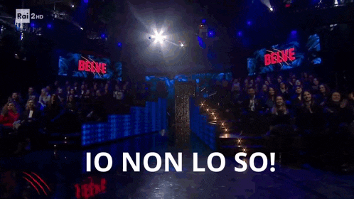 a crowd of people are sitting in front of a stage with the words io non lo so written on it .
