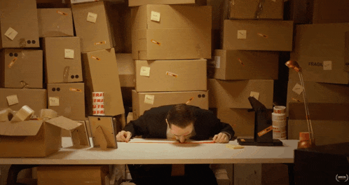 a man sits at a desk surrounded by cardboard boxes with fragile written on them